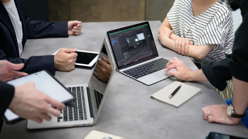 テーブルでノートパソコンとタブレットを囲む4人の手元